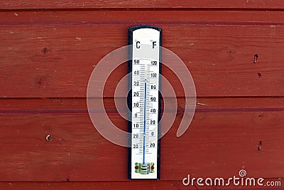 Thermometer displaying high temperatures hanging on a reddish wooden wall Stock Photo