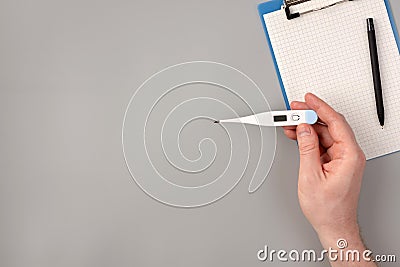 Thermometer in hand, notepad and pen on gray background Stock Photo