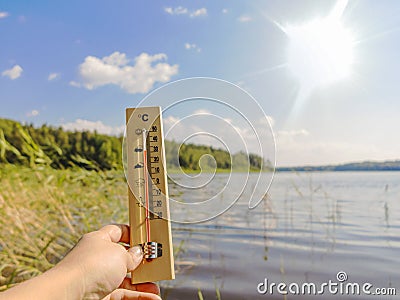 Thermometer showing 30 degrees Celsius of heat against the background of the lake water and the blue sky in sunlight Stock Photo
