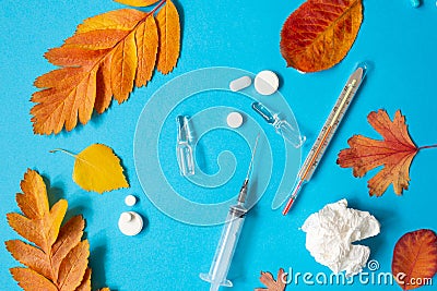 Thermometer, syringe, ampoules, pills, crumpled paper napkin and yellow fallen leaves on blue paper background. Thermometer has Stock Photo