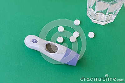 Thermometer with temperature and a handful of tablets and a glass of water on a green background, concept Stock Photo