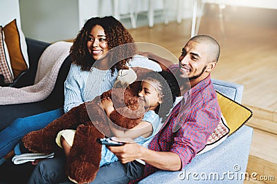 Theyve finally found a great family show. a happy young family of three watching tv together in their living room at Stock Photo