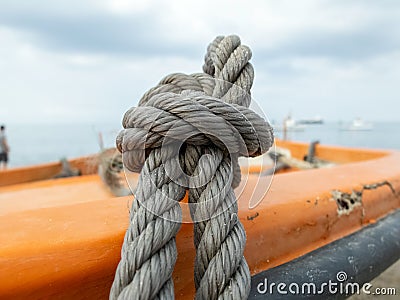 Thick grey rope tied to small orange boat Stock Photo