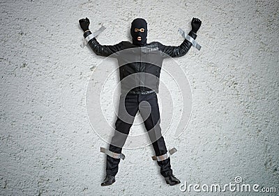 Thief or burglar masked with balaclava is caught and is taped to the wall with duct tape. Stock Photo