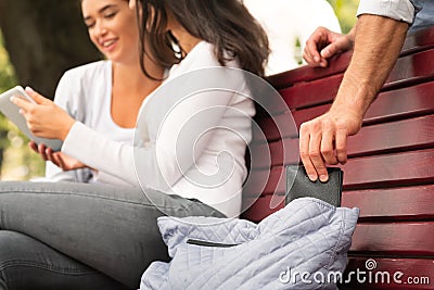 Thief Pickpocketing Wallet While Two Girls Sitting In Park Stock Photo