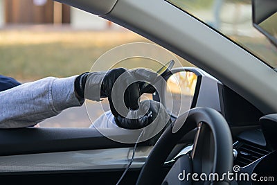 The thief`s hand in a black glove, takes the smartphone from the front of the car, through the open glass, breaking the wire Stock Photo