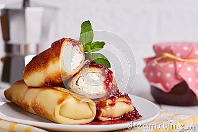 Thin crepe pancake rolls stuffed with cottage cheese, served with raspberry jam. Stock Photo