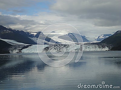 Thin Glacier between two mountains slowly gliding into the pacific ocean with a cloudy backdrop Stock Photo