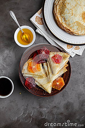 Thin pancakes with honey and blood oranges on a gray table. Stock Photo