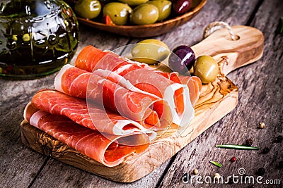 Thin slices of prosciutto with mixed olives on a cutting board Stock Photo