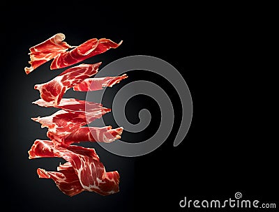 Thin slices of Spanish jamon flying in the air on black background. Traditional meat specialty of the local cuisine Stock Photo