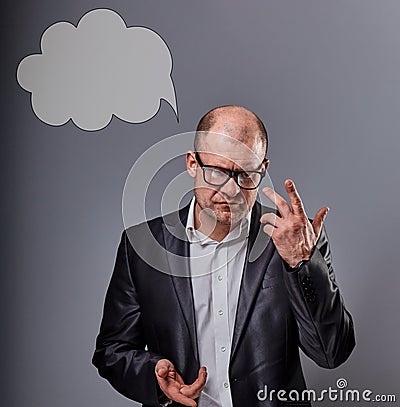 Thinking bald business man in eyeglasses and suit discussing and have an idea on grey background with empty cloud above the head. Stock Photo