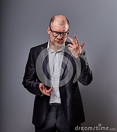 Thinking bald business man in eyeglasses and suit discussing and have an idea on grey background. He looking up and discoursing. Stock Photo