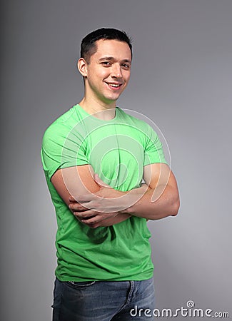 Thinking casual happy smiling young man with folded arms in green t-shirt on grey backgrond Stock Photo