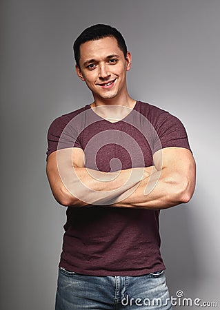 Thinking casual smiling young man with folded strong arms in red t-shirt on grey backgrond Stock Photo