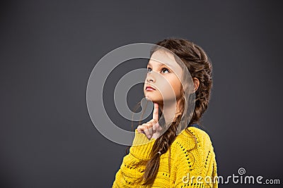 Thinking grimacing serious schoolgirl looking up on grey studio background. Back to school. The concept of education Stock Photo