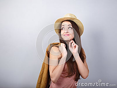 Thinking happy woman in pink t-shirt and suumer straw hat holding leather jacket and looking up on blue background. Closeup Stock Photo