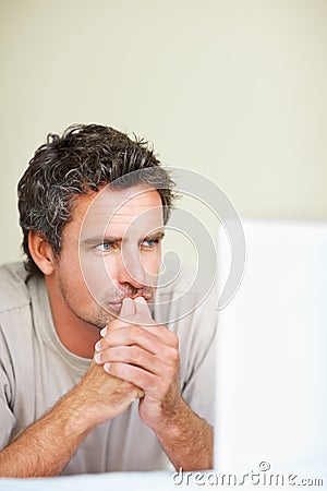 Thinking, man in house and laptop for work from home, serious and sitting alone for freelance job idea. Technology Stock Photo