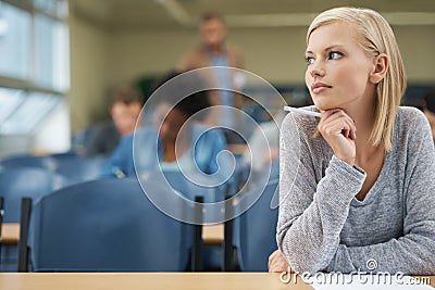 Thinking of the right answer...A pretty blonde student writing exam in a lecture hall. Stock Photo