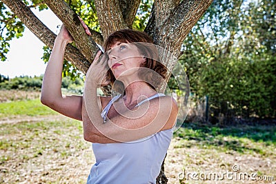 Thinking 50s woman under tree for metaphor of nostalgia Stock Photo