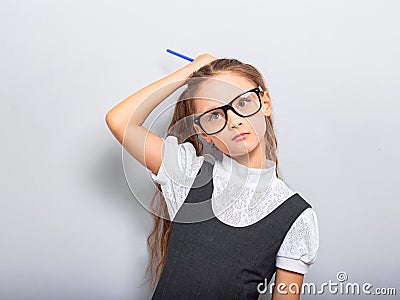 Thinking serious skeptical pupil girl in fashion eyeglasses scratching the pencil the head in school uniform and looking up on Stock Photo