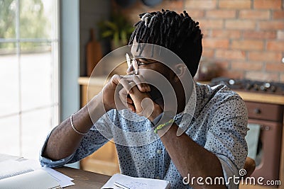 Pensive african male student sit at table reflect on task Stock Photo