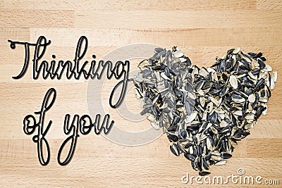 Thinking of you - card. Heart lined with husks of sunflower seeds on a background of beech wood. Stock Photo