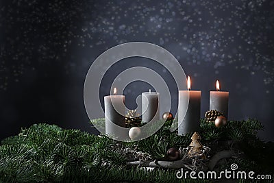 Third advent with three burning candles on fir branches with Christmas decoration against a dark grey background, copy space Stock Photo