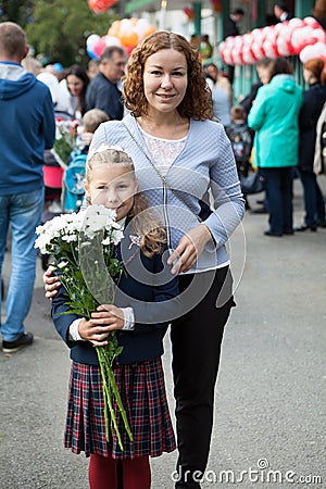 Third-grade girl with bouquet of chamomiles standing in schoolyard with mother, portrait Stock Photo