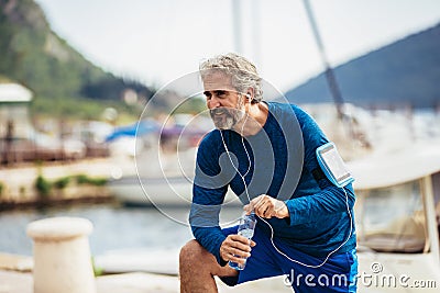 Thirsty senior man drinking water before running. Active old man having a break during his jog routine outside Stock Photo