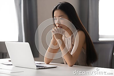 Thoughtful Asian businesswoman looking at laptop screen, pondering task Stock Photo