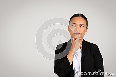 Thoughtful Asian businesswoman with a hand on her chin looking up and away Stock Photo
