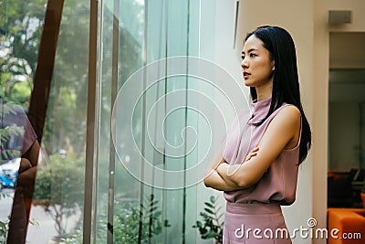 Thoughtful Asian businesswoman looking out of window in modern office Stock Photo