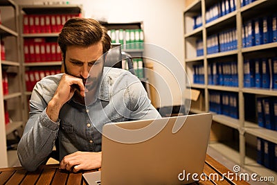 Thoughtful business executive using laptop in file storage room Stock Photo