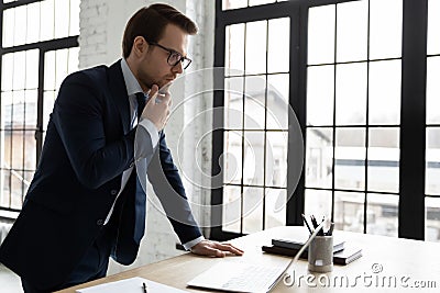 Thoughtful businessman looking at laptop screen, standing at table Stock Photo