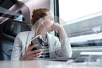 Thoughtful businesswoman listening to podcast on mobile phone while traveling by train. Stock Photo