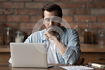 Thoughtful focused man in glasses looking at laptop screen Stock Photo