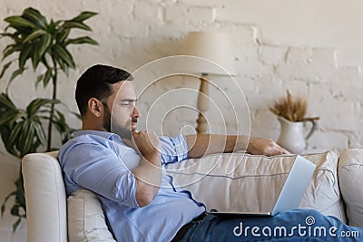 Thoughtful focused young millennial business man using laptop working Stock Photo
