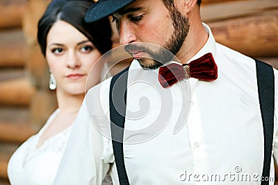 Thoughtful groom in hat with beard, mustache, bow tie and suspenders. Bride wearing white wedding dress. Gangster style. Stock Photo