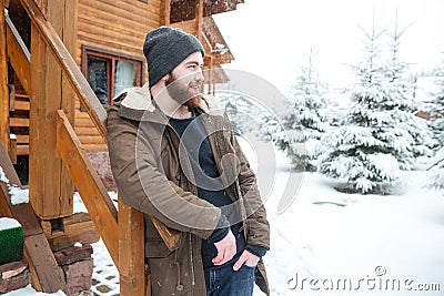 Thoughtful man with beard standing near log cabine in winter Stock Photo