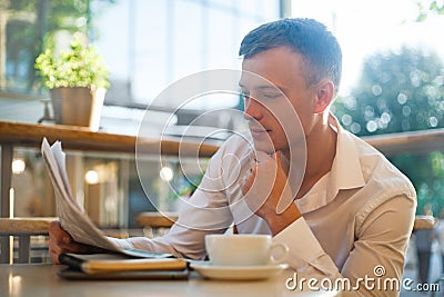 Thoughtful man reading a newspaper in a street cafe at lunch. Stock Photo