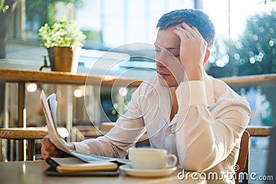 Thoughtful man reading a newspaper in a street cafe at lunch. Stock Photo