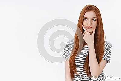 Thoughtful perplexed pondering young redhead blue-eyed woman smirking touching jawline thinking look upper left corner Stock Photo