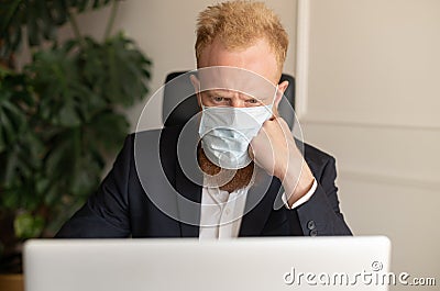 Thoughtful red-haired businessman in smart casual suit wearing protective face mask Stock Photo