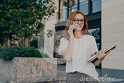 Thoughtful redhead woman looks into distance makes phone call holds smartphone near ear Stock Photo