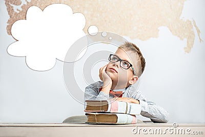 A thoughtful schoolboy sits at a desk with books Stock Photo