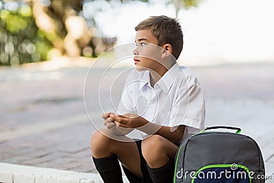 Thoughtful schoolboy sitting alone in campus Stock Photo