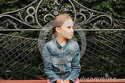 Thoughtful scowl candid eight year old kid girl sits on bench and observe nature. prepubertal age of children and their lives, min Stock Photo