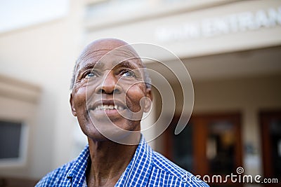 Thoughtful senior man smiling while looking up at nursing home Stock Photo