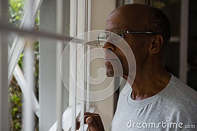 Thoughtful senior man wearing eyeglasses while looking out through window Stock Photo